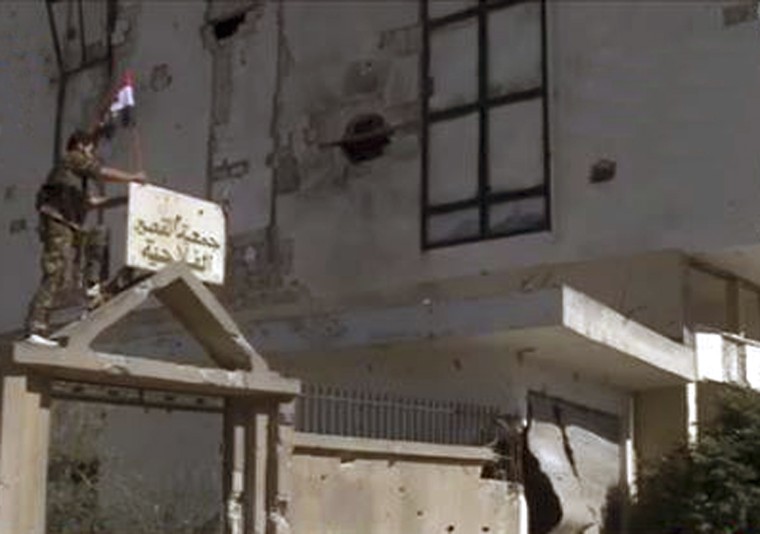 A member of forces loyal to Syria's President Bashar al-Assad erects a Syrian flag atop of a gate in Qusair, in this handout photograph distributed by Syria's national news agency SANA