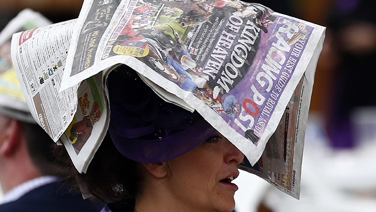 A woman uses a newspaper to protect her hat from the rain during the first day of the Royal Ascot horse racing festival at Ascot